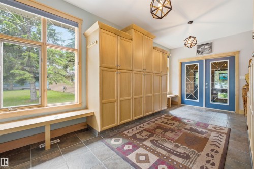 Entryway featuring extensive wood-finish cabinetry, a large window with a built-in bench, two geometric pendant lights, and blue double doors with decorative glass inserts - A38 Bernice Ave, Rural Leduc County, AB 