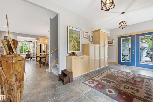 Tile flooring extends into the entryway, featuring extensive built-in cabinetry, dual glass-paneled entry doors, and geometric pendant lighting - A38 Bernice Ave, Rural Leduc County, AB 
