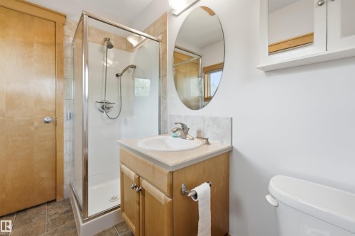 Bathroom with a glass-enclosed shower, wood-finish vanity, light countertop, oval mirror, and tiled flooring - A38 Bernice Ave, Rural Leduc County, AB 