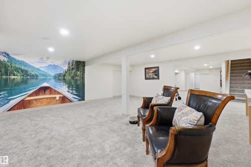 Spacious finished room featuring a scenic wall mural, light-colored carpeting, recessed lighting, and a visible staircase - A38 Bernice Ave, Rural Leduc County, AB 