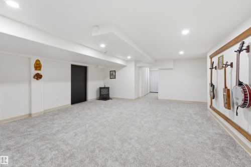 Finished lower level featuring light gray carpeting, recessed lighting, white walls, a black interior door, and a freestanding stove - A38 Bernice Ave, Rural Leduc County, AB 