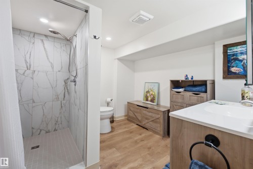 Bathroom featuring a walk-in shower with large format marble-look tile, a white toilet, and wood-finish flooring - A38 Bernice Ave, Rural Leduc County, AB 