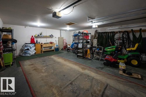 Spacious garage featuring concrete flooring, track lighting, an overhead garage door opener, and integrated wall shelving - A38 Bernice Ave, Rural Leduc County, AB 