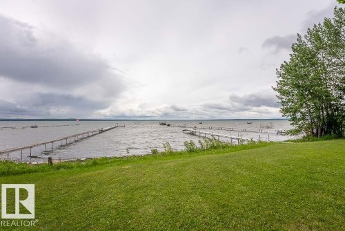 Expansive waterfront property featuring a large grassy area, numerous mature trees, and multiple wooden docks extending into the water - A38 Bernice Ave, Rural Leduc County, AB 