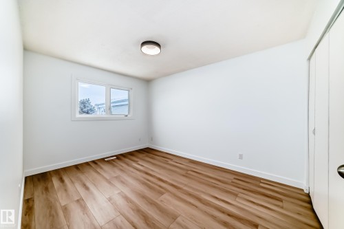 Bright room featuring a window with white trim, wood-finish flooring, a contemporary flush-mount ceiling light, and a white bi-fold closet door - 9D Castle Terrace, Edmonton, AB 