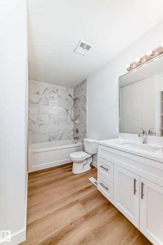 Bathroom featuring wood-finish flooring, a white vanity with an integrated sink, a large wall-mounted mirror, a tub-shower combination with marble-look tile surround, and a ceiling-mounted exhaust fan - 9D Castle Terrace, Edmonton, AB 