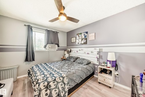 Bedroom featuring wood-finish flooring, a window with dark curtains, and a ceiling fan with integrated lighting - 5106 19 Avenue, Edmonton, AB 