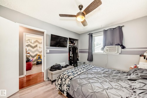 Bedroom featuring a ceiling fan with integrated lighting, wall-mounted television, and a window with an individual air conditioning unit - 5106 19 Avenue, Edmonton, AB 