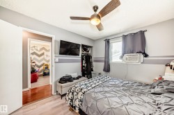 Bedroom featuring a ceiling fan with integrated lighting, wall-mounted television, and a window with an individual air conditioning unit - 