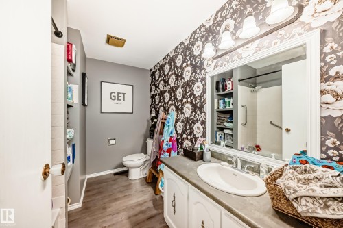 Bathroom featuring wood-finish flooring, a vanity with an integrated sink, and floral-patterned wallpaper - 5106 19 Avenue, Edmonton, AB 