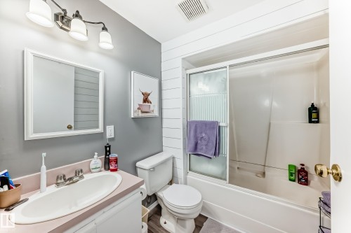 Bathroom featuring a vanity with an integrated sink, a framed wall mirror, a three-bulb vanity light fixture, and a tub/shower combination with a sliding glass door - 5106 19 Avenue, Edmonton, AB 