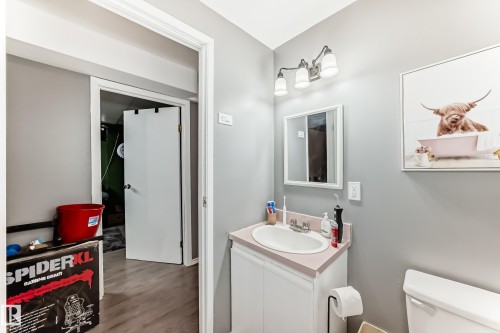 Bathroom featuring a white vanity cabinet with an integrated sink and light-toned countertop, a wall-mounted mirror, and a three-light fixture - 5106 19 Avenue, Edmonton, AB 