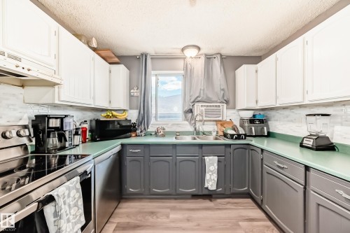 Kitchen featuring two-tone cabinetry with white upper cabinets and gray lower cabinets, a light green countertop, and a white subway tile backsplash - 5106 19 Avenue, Edmonton, AB 