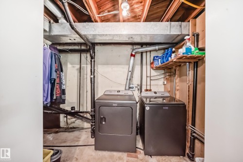 Dedicated laundry area featuring a washer and dryer set, exposed wood ceiling joists, and a metal HVAC duct - 5106 19 Avenue, Edmonton, AB 