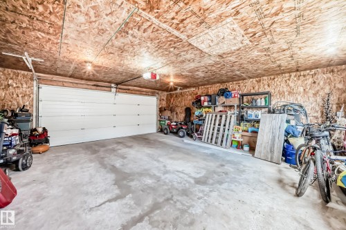 Spacious attached garage featuring a wide white sectional garage door, concrete flooring, exposed oriented strand board walls, and overhead lighting - 5106 19 Avenue, Edmonton, AB 