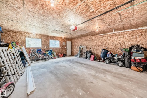 Spacious garage featuring a concrete floor, exposed OSB walls and ceiling, multiple windows, overhead lighting, and an overhead garage door opener mechanism - 5106 19 Avenue, Edmonton, AB 