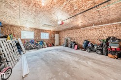 Spacious garage featuring a concrete floor, exposed OSB walls and ceiling, multiple windows, overhead lighting, and an overhead garage door opener mechanism - 