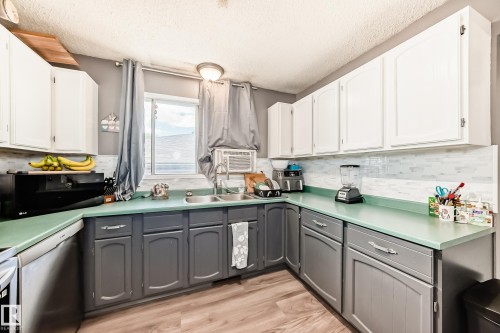 Kitchen featuring white upper cabinetry, gray lower cabinetry, light green countertops, a white subway tile backsplash, and wood-finish flooring - 5106 19 Avenue, Edmonton, AB 