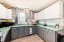 Kitchen featuring white upper cabinetry, gray lower cabinetry, light green countertops, a white subway tile backsplash, and wood-finish flooring - 5106 19 Avenue, Edmonton, AB 