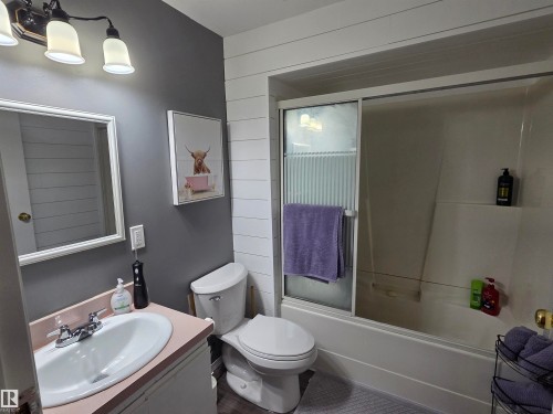 Bathroom featuring a white vanity with a pink countertop, a white toilet, and a combination tub and shower with sliding glass doors - 5106 19 Avenue, Edmonton, AB 