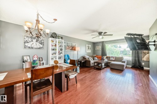 Open-concept living space featuring wood-finish flooring, a contemporary chandelier, and a ceiling fan - 5106 19 Avenue, Edmonton, AB 