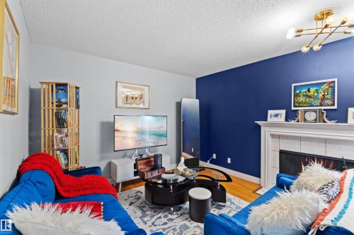 Living area featuring wood-finish flooring, a decorative fireplace with a white mantel, and a multi-directional ceiling light fixture - 12128 25 Avenue, Edmonton, AB - Indoor Photo Showing Bedroom