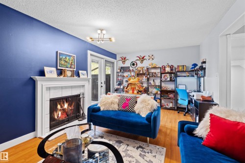 Living area featuring a traditional fireplace with white mantel, glass sliding door, and wood-finish flooring - 12128 25 Avenue, Edmonton, AB - Indoor Photo Showing Living Room With Fireplace