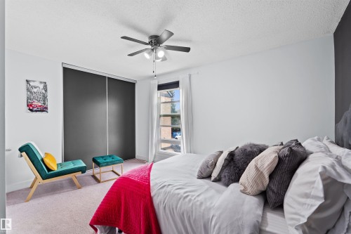 Bedroom featuring a ceiling fan with integrated lighting, a window with white drapes, and a built-in wardrobe with dark sliding doors - 12128 25 Avenue, Edmonton, AB - Indoor Photo Showing Bedroom