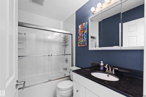 Bathroom featuring a white vanity with brushed nickel hardware, a dark countertop, and an oval undermount sink - 12128 25 Avenue, Edmonton, AB - Indoor Photo Showing Bathroom