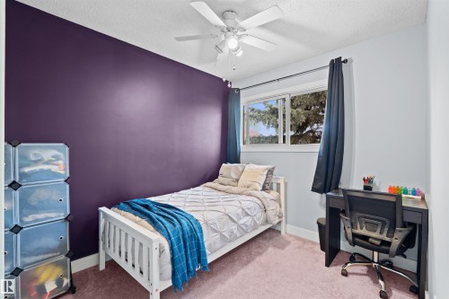 Bedroom featuring a window with exterior tree views, a ceiling fan with integrated lighting, and a neutral carpeted floor - 12128 25 Avenue, Edmonton, AB - Indoor Photo Showing Bedroom