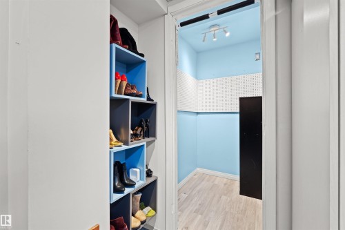 Walk-in closet featuring light blue walls, light wood-finish flooring, white pegboard panels, and recessed track lighting - 12128 25 Avenue, Edmonton, AB - Indoor Photo Showing Other Room