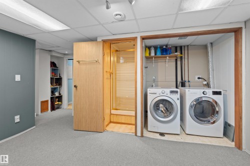 Dedicated laundry area featuring front-loading washer and dryer units, overhead shelving, and a drop ceiling - 12128 25 Avenue, Edmonton, AB - Indoor Photo Showing Laundry Room