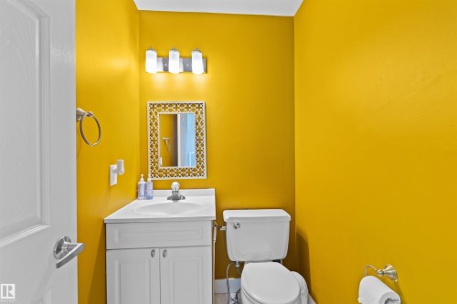 Bathroom featuring a white vanity with integrated sink, a mirror with an ornate frame, a chrome faucet, and a three-light vanity fixture - 12128 25 Avenue, Edmonton, AB - Indoor Photo Showing Bathroom