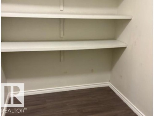 Built-in shelving unit with two white shelves, neutral-toned walls, dark wood-finish flooring, and white baseboards - 107 10023 164St, Edmonton, AB 