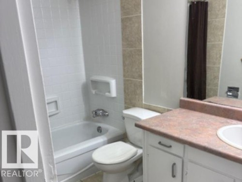 Bathroom featuring a white tub, white tiled surround, and a vanity with an integrated sink and countertop - 107 10023 164St, Edmonton, AB 