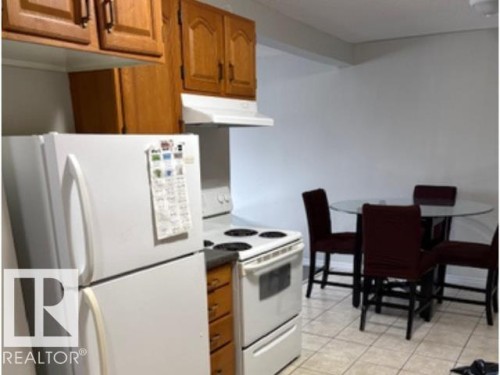 Kitchen featuring wood cabinetry, white appliances, and tiled flooring - 107 10023 164St, Edmonton, AB 