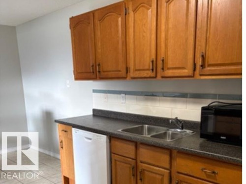 Kitchen featuring wood cabinetry with arched top panels, dark speckled countertops, and a white subway tile backsplash - 107 10023 164St, Edmonton, AB 