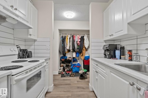 Galley-style kitchen featuring white cabinetry, solid surface countertops, and an electric range - 115 4608 52 Avenue, Stony Plain, AB 
