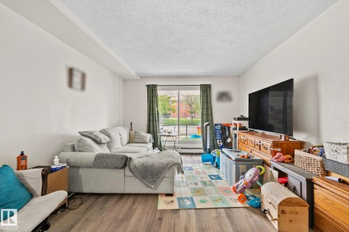 Spacious living area featuring wood-finish flooring and a large window with vertical blinds - 115 4608 52 Avenue, Stony Plain, AB 