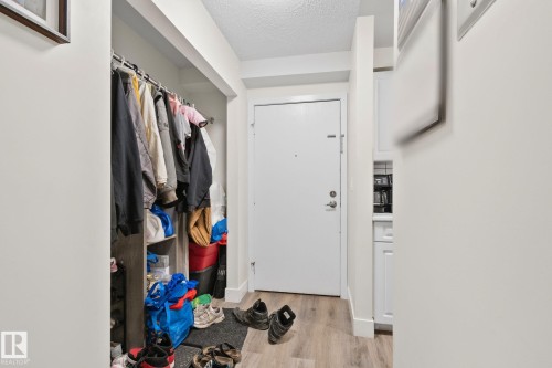 Entryway featuring wood-finish flooring, a white paneled door with polished chrome hardware, and a recessed closet with built-in shelving - 115 4608 52 Avenue, Stony Plain, AB 