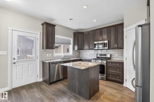 Modern kitchen featuring dark wood-finish cabinetry, granite countertops, and stainless steel appliances - 6927 Cardinal Wynd, Edmonton, AB 