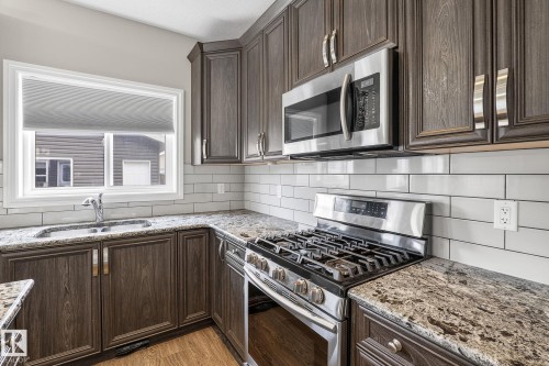 Kitchen featuring wood-finish cabinetry, speckled countertops, and a white subway tile backsplash - 6927 Cardinal Wynd, Edmonton, AB 