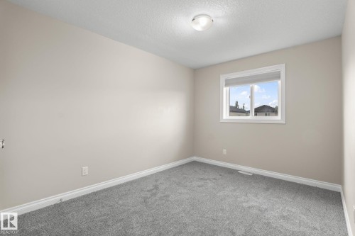Carpeted room featuring a double-paned window, neutral wall paint, white baseboards, and a flush-mount ceiling light - 6927 Cardinal Wynd, Edmonton, AB 