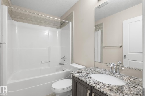 Bathroom featuring a white tub/shower combination, decorative tile surround, dark wood-finish vanity with an undermount sink, and a speckled countertop - 6927 Cardinal Wynd, Edmonton, AB 