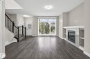 Spacious living area featuring wood-finish flooring, a contemporary fireplace with a tiled surround, built-in shelving, and a large window with vertical blinds - 6927 Cardinal Wynd, Edmonton, AB 