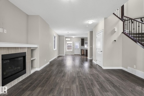Open-concept living area featuring wood-finish flooring, a tiled fireplace with integrated shelving, and neutral wall tones - 6927 Cardinal Wynd, Edmonton, AB 