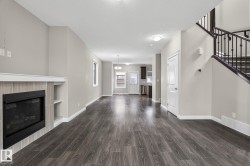 Open-concept living area featuring wood-finish flooring, a tiled fireplace with integrated shelving, and neutral wall tones - 