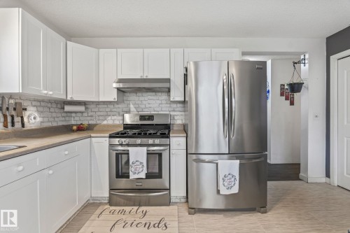 Kitchen featuring stainless steel appliances, white cabinetry, light-toned countertops, and a white brick-patterned backsplash - 128 Brookview Wy, Stony Plain, AB 