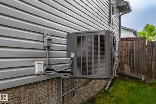 Exterior vinyl siding with a foundation featuring a textured finish, accompanied by a side yard with a wood fence - 128 Brookview Wy, Stony Plain, AB 