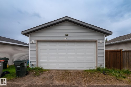 Detached garage featuring light grey vinyl siding, a dark shingle roof, and a panel garage door - 128 Brookview Wy, Stony Plain, AB 